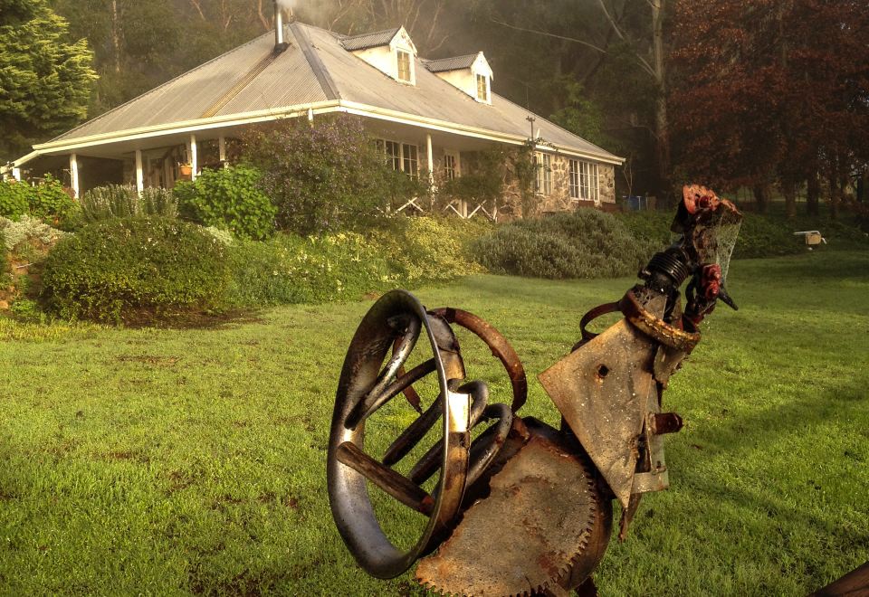 a black horse - drawn carriage with a person driving it in the distance , surrounded by green grass and trees at Balingup Heights Hilltop Forest Cottages