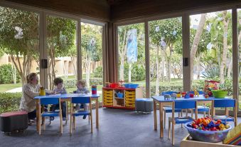 a group of children playing in a room with blue tables and chairs , surrounded by windows that allow natural light to fill the space at Dusit Thani LakeView Cairo