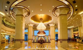 a grand hotel lobby with two tall columns , a large chandelier hanging from the ceiling , and a television mounted on the wall at City Hotel