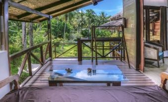a wooden deck with a glass table and chairs , overlooking a lush green landscape and palm trees at Janji Laut Resort