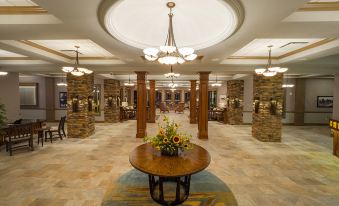 a grand hotel lobby with marble floors , large columns , and a wooden round table surrounded by flowers at Chautauqua Harbor Hotel - Jamestown