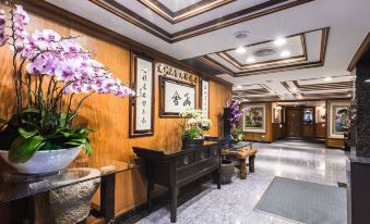 a room with wooden walls , a table with a vase of flowers on it , and paintings hanging on the wall at Han She Business Hotel