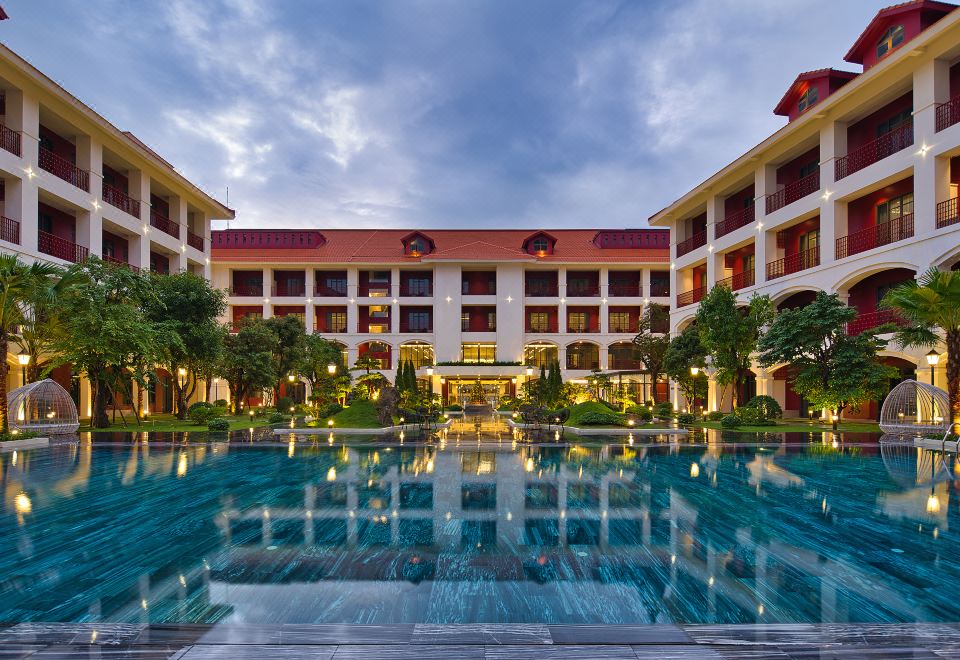 a large hotel building with a swimming pool in front of it , surrounded by trees and grass at Senna Hue Hotel