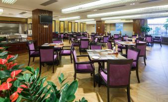 a dining room with purple chairs and tables , a television on the wall , and green plants at City Hotel