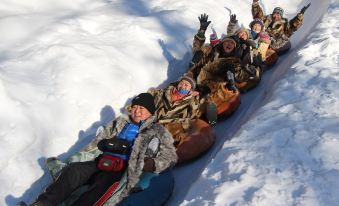 Children are sledding down a snowy hill while other kids watch from the ground at Xiaoguo Travellers' Home