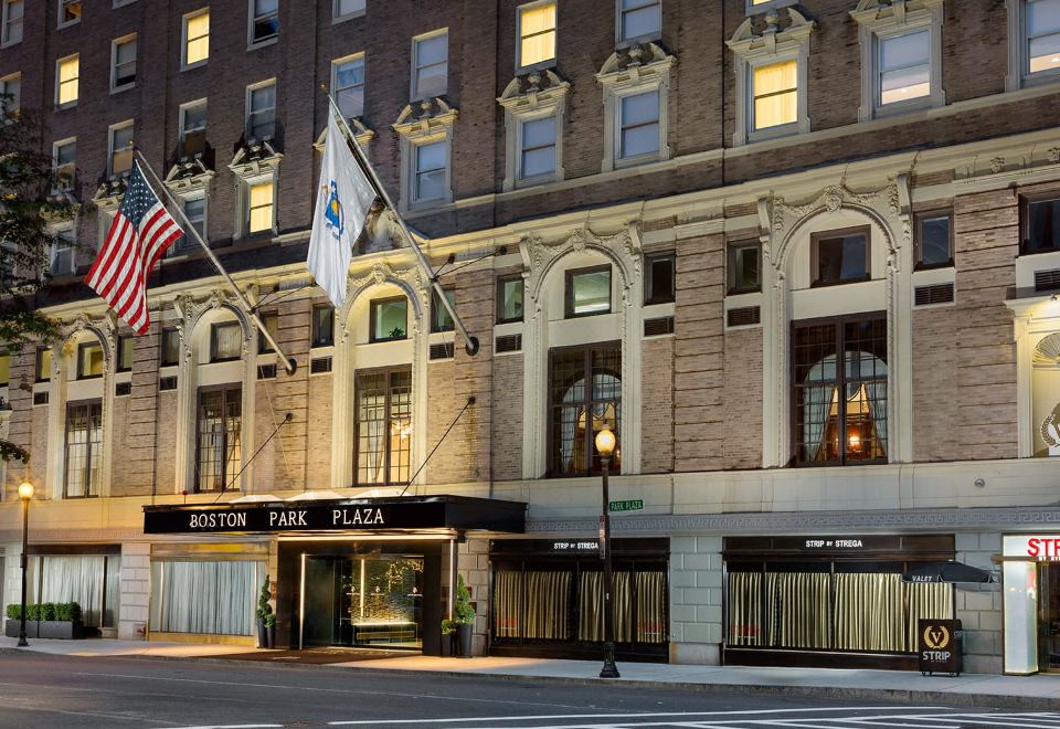 the exterior of a hotel named roston park plaza , with its entrance lit up at night and american and european flags hanging from the windows at Hilton Boston Park Plaza