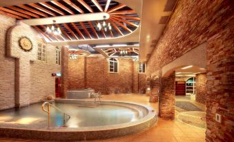 a large indoor swimming pool with a wooden roof and stone walls is surrounded by glass railings at Huis Ten Bosch