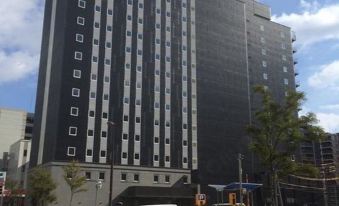 a tall , black and white building with a parking lot in front of it , under a cloudy sky at Hotel Monte Hermana Fukuoka