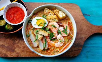 a bowl of noodles on a wooden table , accompanied by a spoon and a cup at Sun Inns Hotel Ayer Keroh