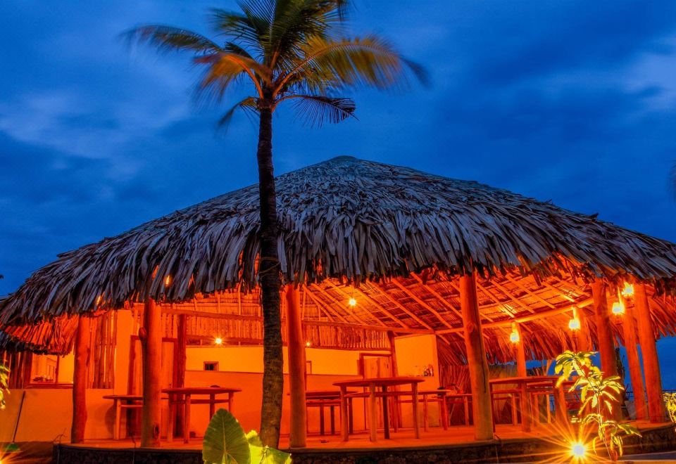 a tiki hut with a thatched roof , surrounded by palm trees and lit up at night at Royal Beach