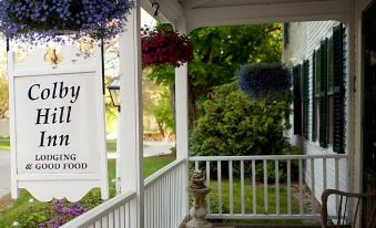 "a porch with a sign reading "" colby hill inn "" and hanging flowers , inviting visitors to enjoy the view" at Colby Hill Inn