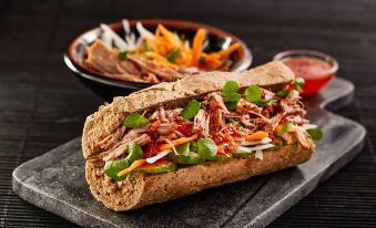 a sandwich with meat and vegetables is on a black stone plate next to a bowl of salad at Helen Browning's Royal Oak