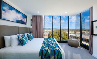 a large bed with a colorful blanket is in a room with a window overlooking the city at Mantra Albury Hotel