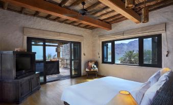 a bedroom with a bed , television , and sliding glass doors leading to an outdoor balcony at Six Senses Zighy Bay