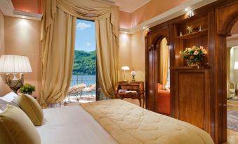 a bedroom with a large bed , white sheets , and a view of a lake through the window at Grand Hotel Tremezzo