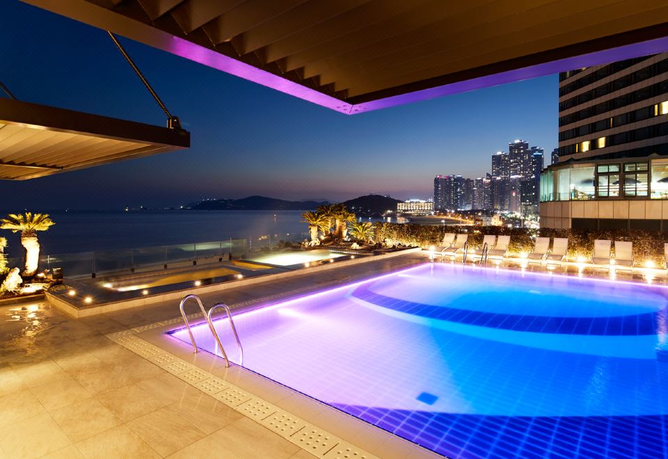 an outdoor pool with a view of the city skyline at night , illuminated by purple lights at Paradise Hotel Busan