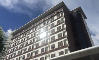 a tall white building with many windows is shown against a blue sky with clouds at HIG Hotel