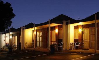 a building with a covered patio and lights on , including chairs and tables , at night at Cameron Thermal Motel