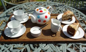 a wooden tray filled with various breakfast items , including cups , saucers , and a teapot , placed on a table in a backyard setting at Moor Court Farm