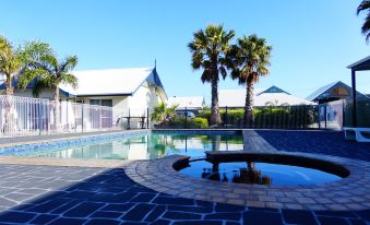 a large outdoor swimming pool surrounded by palm trees , with several lounge chairs and umbrellas placed around the pool area at Torquay Tropicana Motel