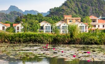 a small pond surrounded by lush greenery , with several houses situated on a hillside nearby at Tam Coc La Montagne Resort & Spa