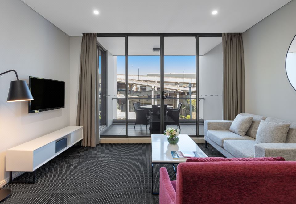 a modern living room with a large window , a couch , and a dining table in the background at Meriton Suites North Ryde