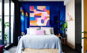 a modern bedroom with a blue and orange abstract painting on the wall , a wooden bed , and various decorative elements at The Cullen Melbourne - Art Series
