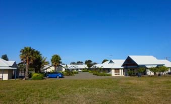 a blue car is parked in a grassy field with houses and palm trees in the background at Torquay Tropicana Motel