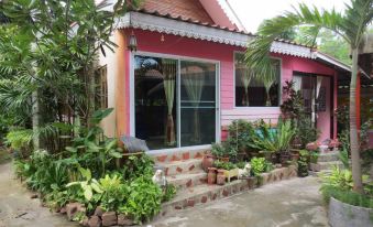 a pink house surrounded by a lush garden , with various plants and trees in the yard at Baan Ton Nam Resort SuanPhueng