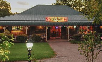 "a restaurant named "" steak house "" with a red sign on the side , and it is lit up at night" at Rest Point Motor Inn