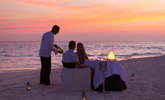 a man and a woman are sitting at a table on the beach , enjoying a romantic dinner at Meeru Maldives Resort Island