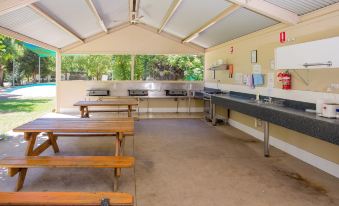 an outdoor kitchen area with a sink , stove , and tables under a covered roof , providing a comfortable outdoor space for cooking at Shepparton Holiday Park and Village
