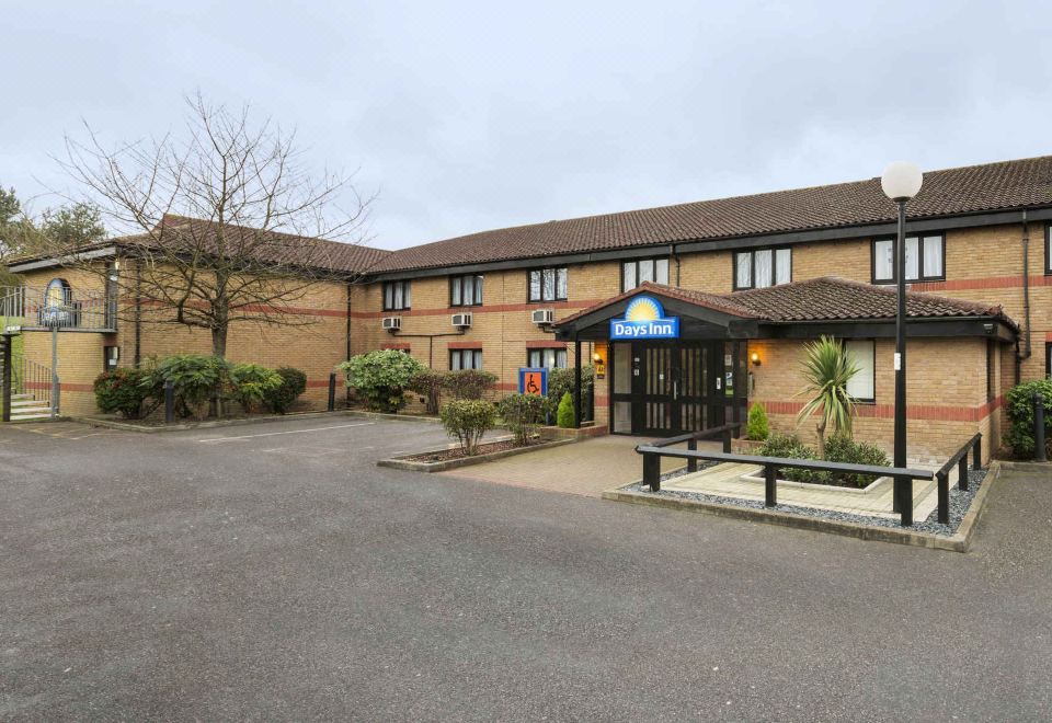 a days inn hotel with a blue and gold sign , surrounded by trees and cars in the driveway at Days Inn by Wyndham London Stansted Airport