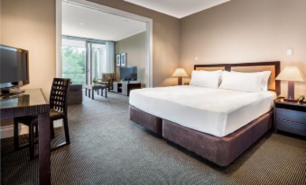 a large bed with white linens is in a room with a chair , table , and sliding glass door at Hilton Lake Taupo