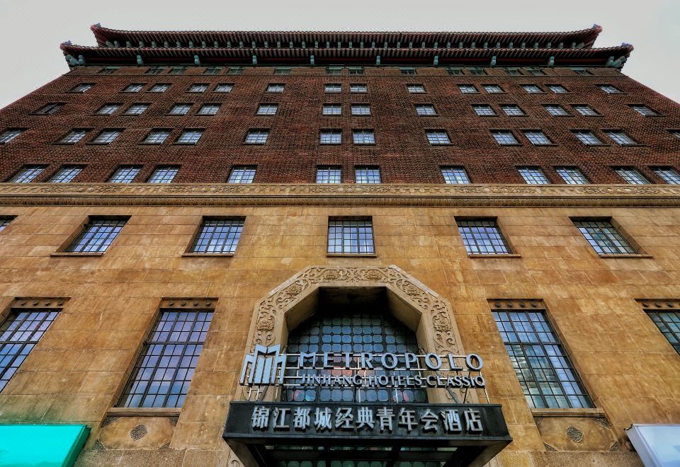 The front entrance of a hotel is adorned with an oriental sign, while another building stands nearby at Metropolo Jinjiang Hotels Classiq (Shanghai Qingnianhui People's Square)