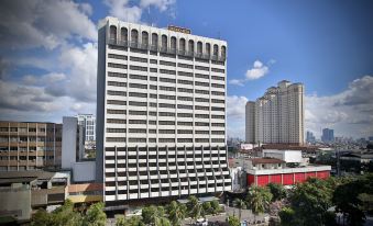 a tall white building in the middle of a city , surrounded by other buildings and trees at Jayakarta Hotel Jakarta