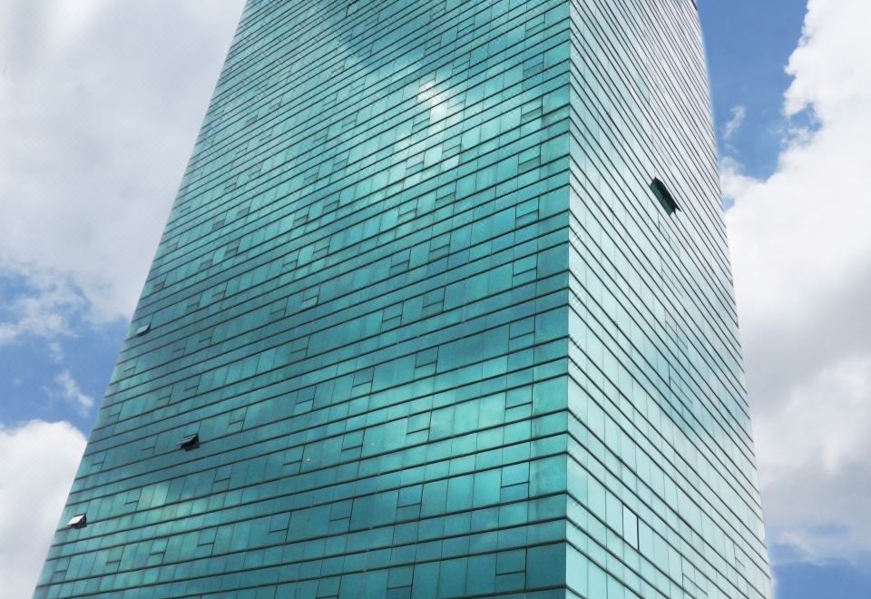 a tall , modern building with a blue glass facade is set against a cloudy sky at Bay Hotel Srinakarin