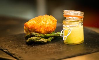 a plate with a fried chicken piece , asparagus , and a jar of yellow sauce on a black surface at The Nags Head