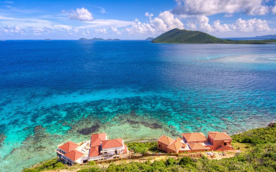 a picturesque view of a tropical island with clear blue water and a red - roofed resort nestled in the middle at Scrub Island Resort, Spa & Marina