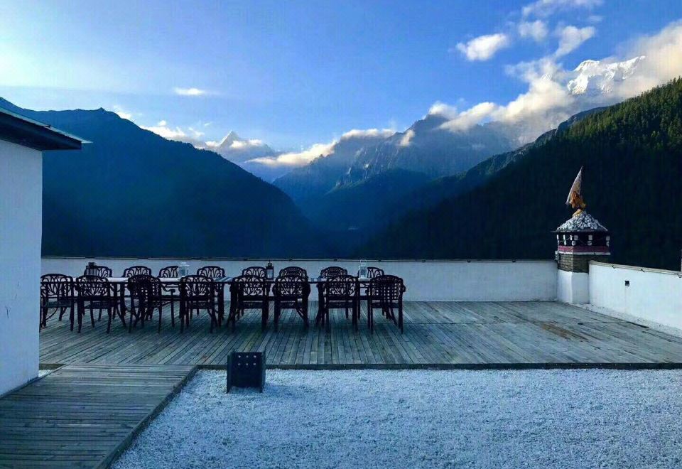 There is a deck with chairs and tables that overlooks the water in front and has mountains behind it on top at Hotel Blanche