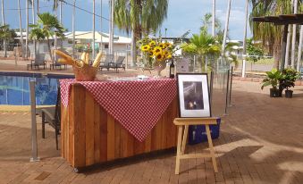 a wooden table with a red and white checkered tablecloth , sunflowers , and a framed picture on it at Club Tropical Resort Darwin