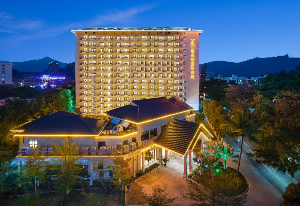 A night view of the hotel at dusk, with illuminated lights and buildings in the background at Vienna International Hotel (Baoting Center)