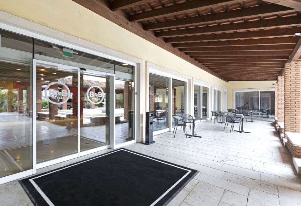 an indoor area with a black rug on the floor and chairs and tables outside at B&B Hotel Affi - Lago di Garda