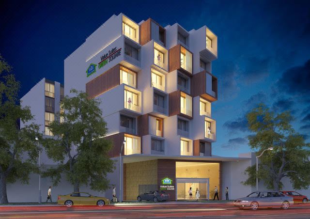 a modern building with multiple floors , lit up at night , and people walking on the street in front of it at ValueSuites Green Square