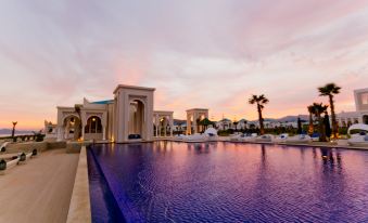 a large blue pool is surrounded by a hotel with multiple buildings and palm trees at Banyan Tree Tamouda Bay