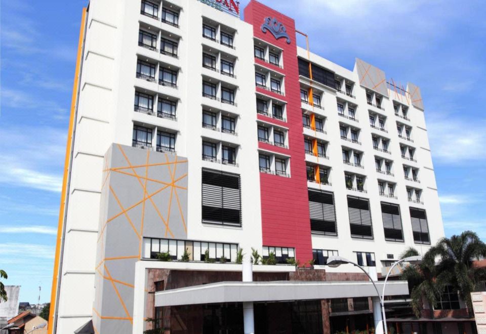 a large hotel with a red and white sign on top of it , located in a city setting at Grand Pasundan Convention Hotel