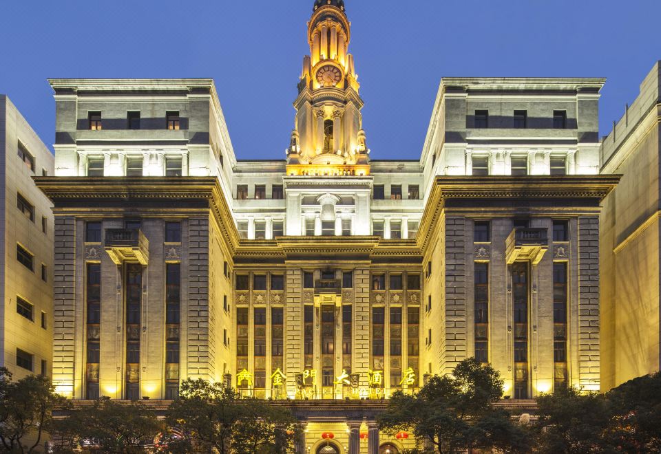 The front view of a large, ornate building with numerous windows is shown at night at Pacific Hotel