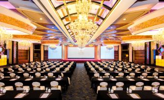 a large conference room with rows of tables and chairs , a chandelier , and a screen at Central Hotel