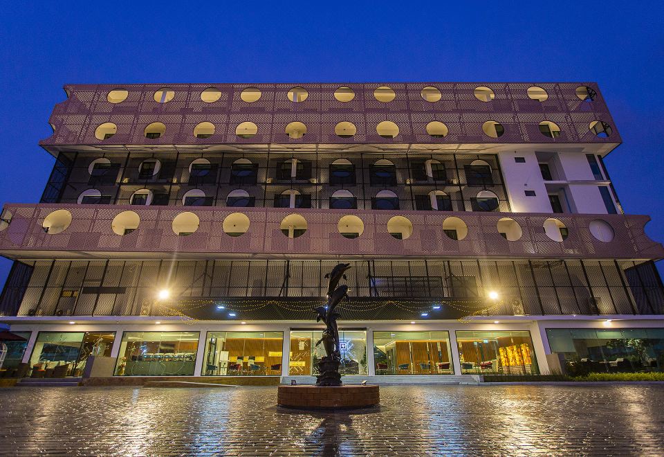 a modern building with multiple floors , surrounded by trees and lit up at night , and a statue in the center of the courtyard at Hotel Fuse Rayong