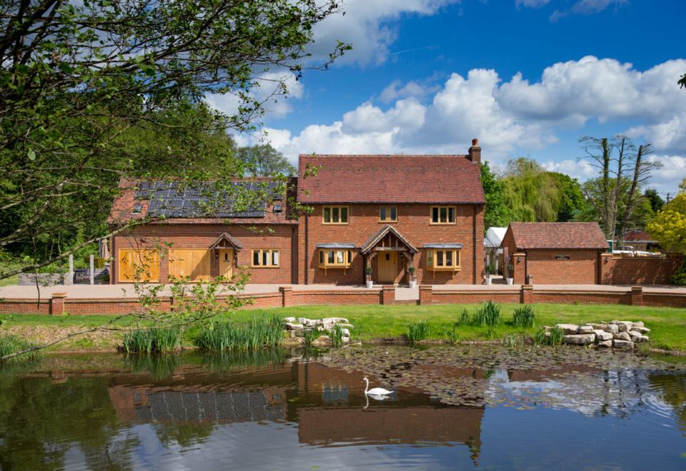 a brick building surrounded by trees and grass , with a pond in the foreground and a swan swimming nearby at Tewinbury